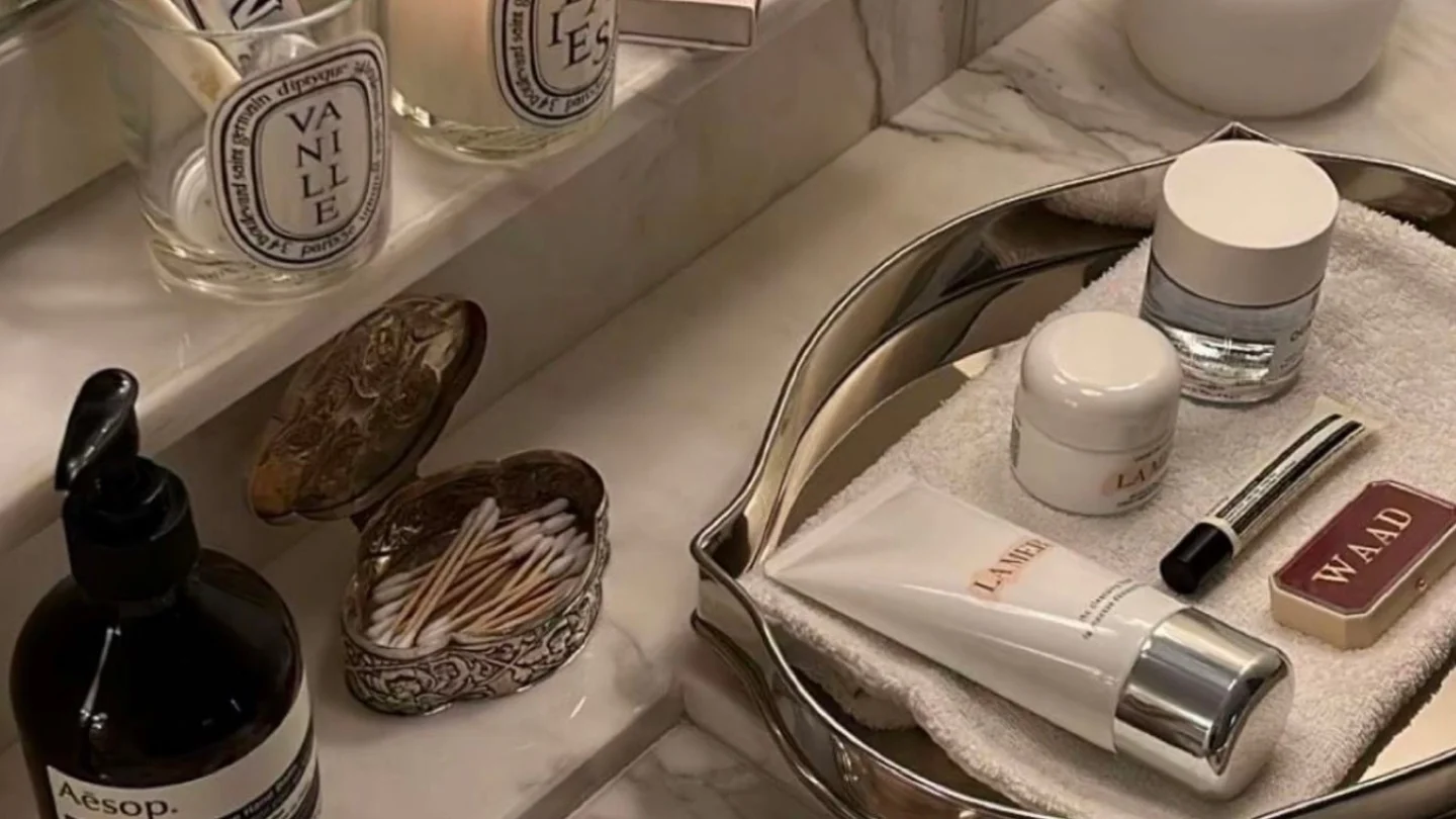 A bathroom sink photographed as is, cluttered with bottles, jars and scented candles.